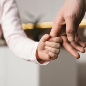 child's hand holding onto adult finger