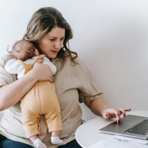 Woman holding baby while using laptop