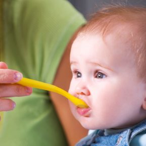 Close up of a young baby with a yellow plastic spoon in his mouth
