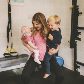 Woman holding two small children around exercise equipment