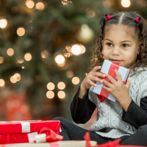 child holding a wrapped present in front of a Christmas tree