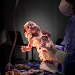 a newborn baby being held in two hands in a hospital room