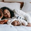Woman lying on a bed behind her sleeping baby