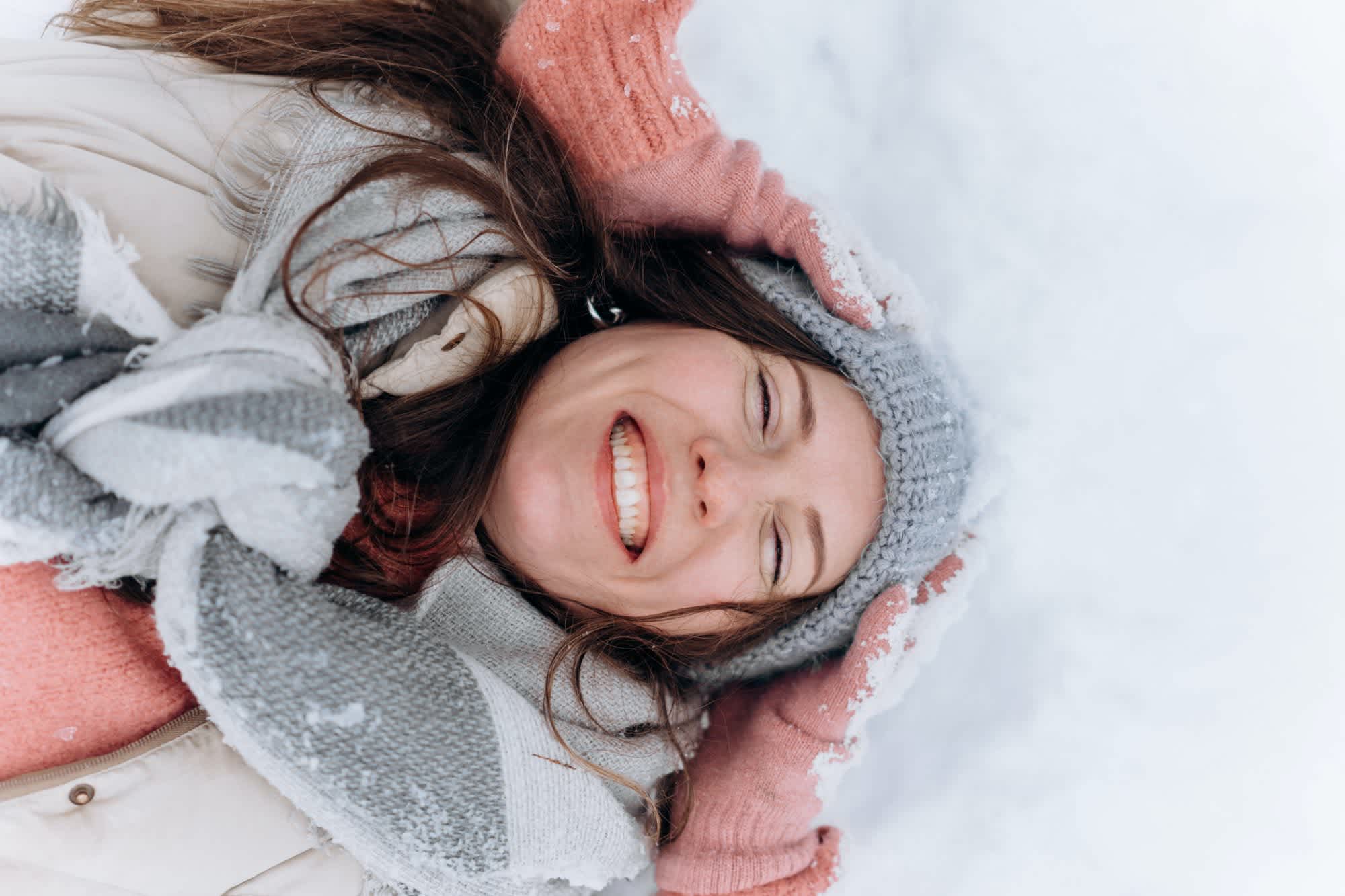 Woman lying in the snow, smiling with her hands on her head