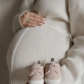 Pregnant woman holding baby shoes in front of her bump