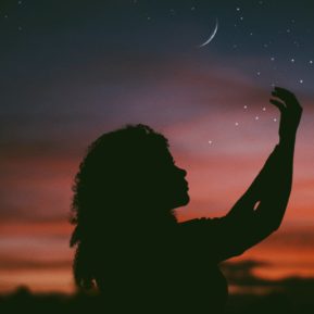 Silhouette of woman holding her hands up to the moon