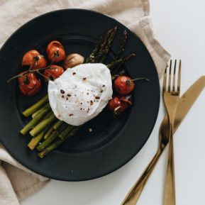 A black bowl with a poached egg, tomatoes and asparagus inside