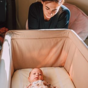 woman looking into her baby's crib at her baby
