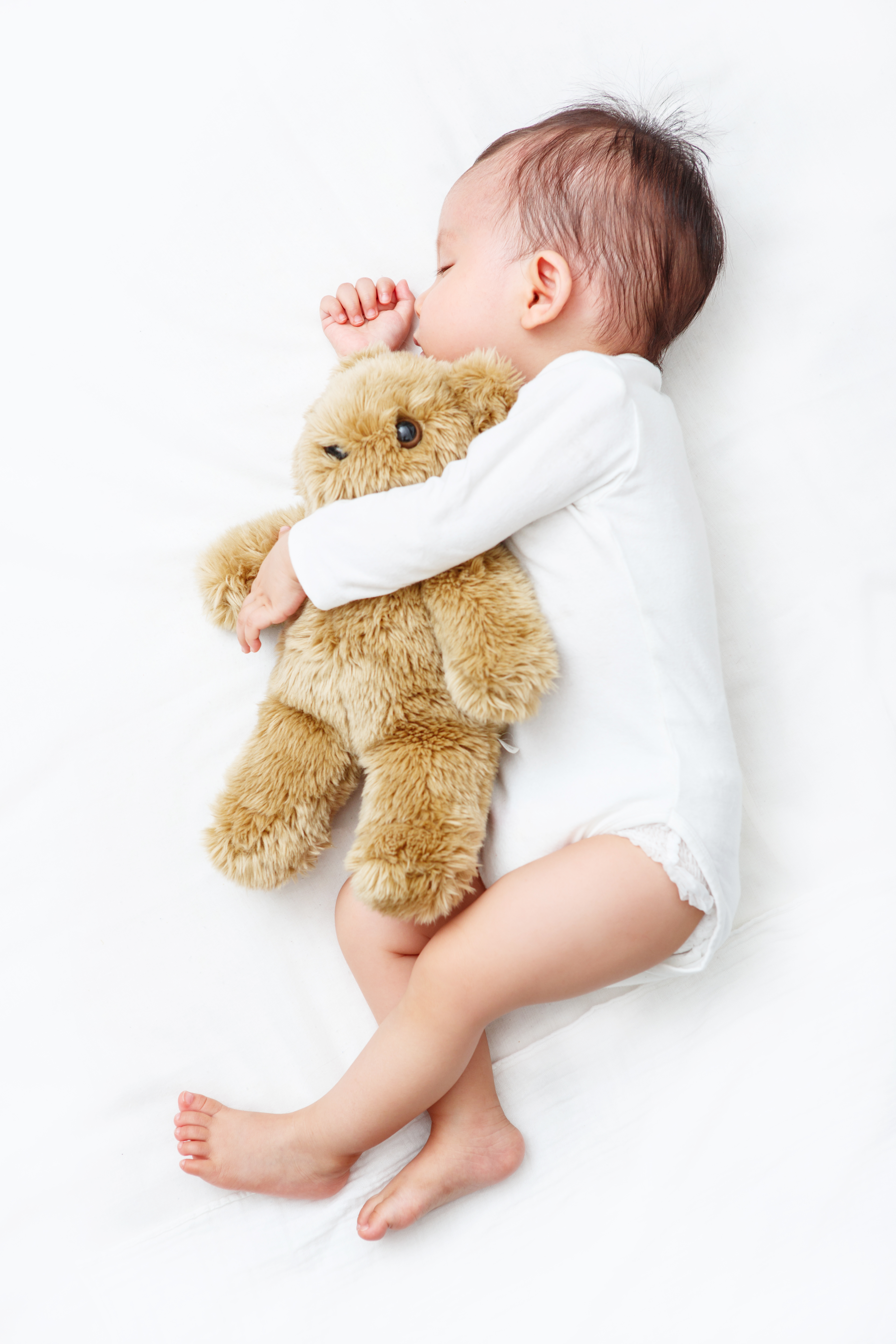 baby lying on side cuddling teddy