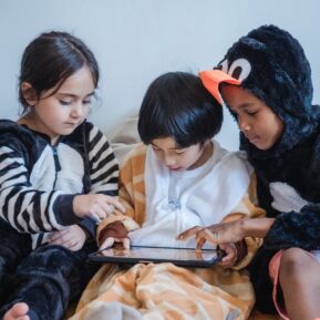 Three children sit on sofa to play on the I pad